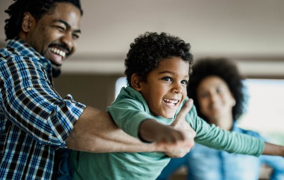 Image of father holding child with mom in the background.